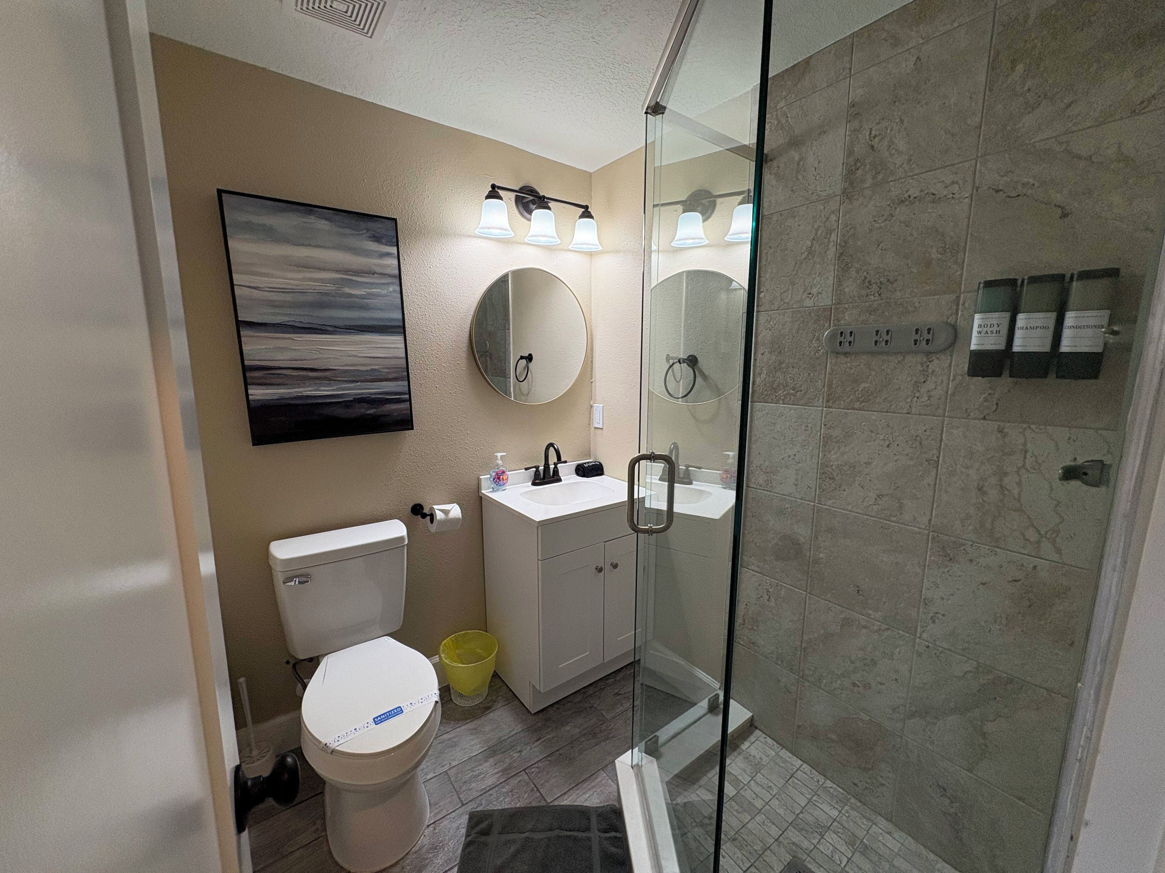 A modern bathroom with a toilet, sink, mirror, and shower.