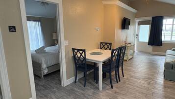 Une pièce comprenant un lit, une table à manger avec des chaises, un ventilateur de plafond et un téléviseur.