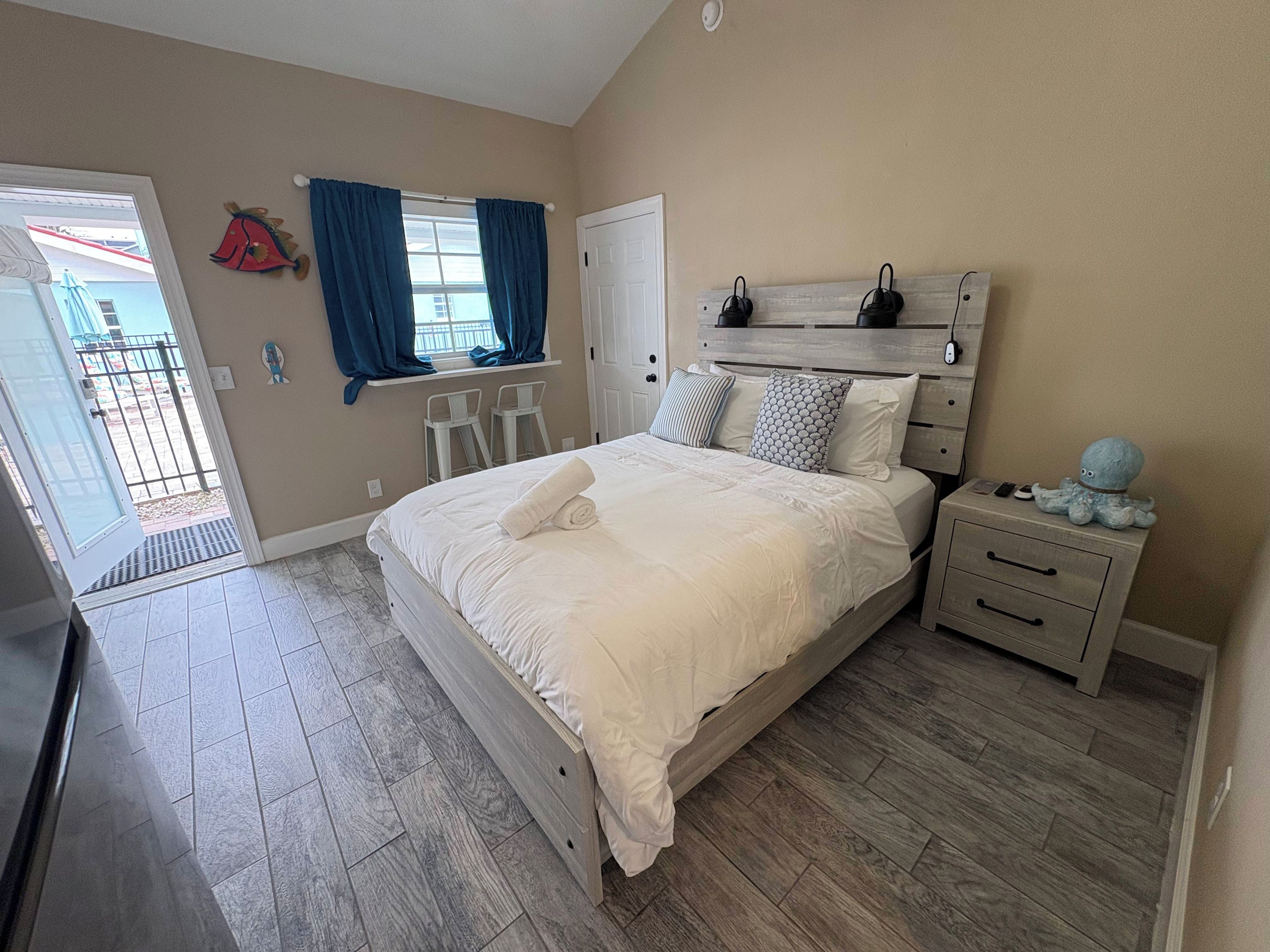 A bedroom with a bed, bedside tables, a window with curtains, a door, and a small balcony visible through the door.