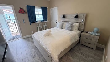 A bedroom with a bed, bedside tables, a window with curtains, a door, and a small balcony visible through the door.