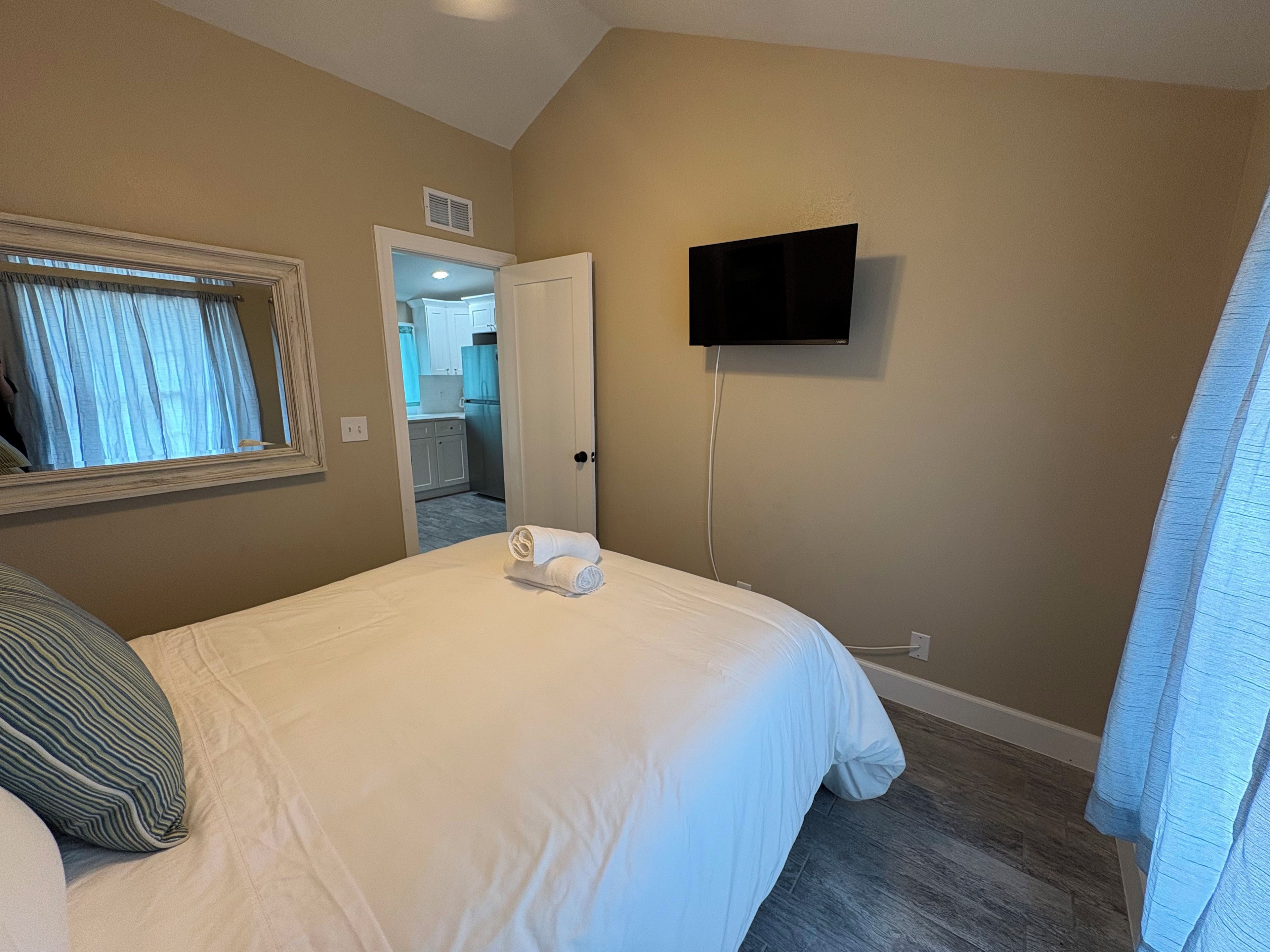 Une chambre d’hôtel avec un lit, un téléviseur fixé au mur et une porte donnant sur une salle de bain.