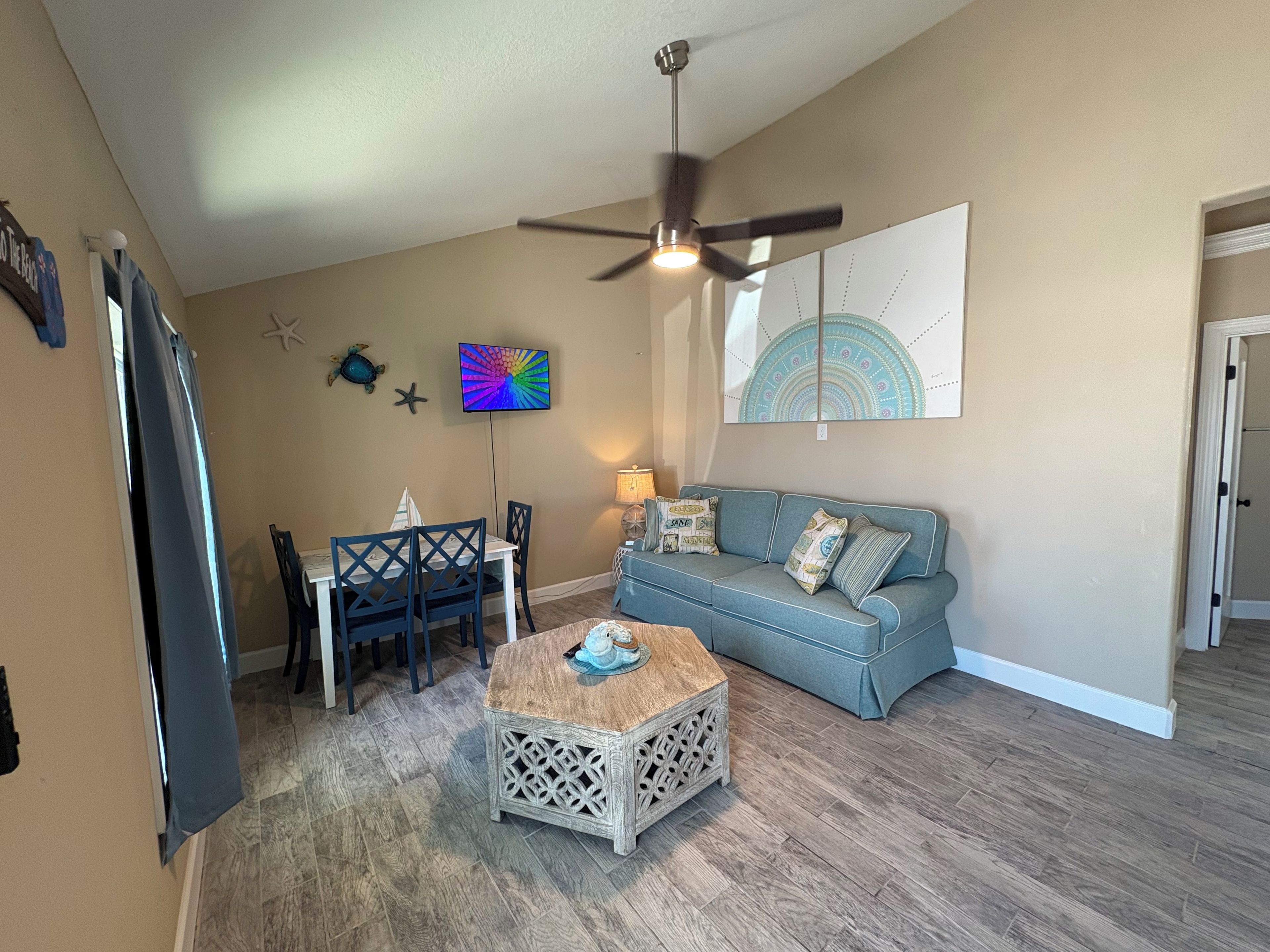 Un salon avec un ventilateur de plafond, une table à manger avec des chaises, un canapé bleu et une table basse.