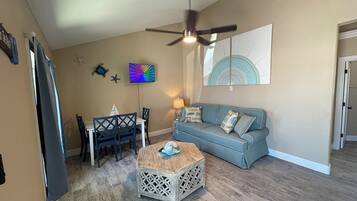Un salon avec un ventilateur de plafond, une table à manger avec des chaises, un canapé bleu et une table basse.