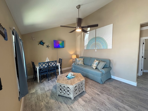 A living room with a ceiling fan, a dining table with chairs, a blue sofa, and a coffee table.