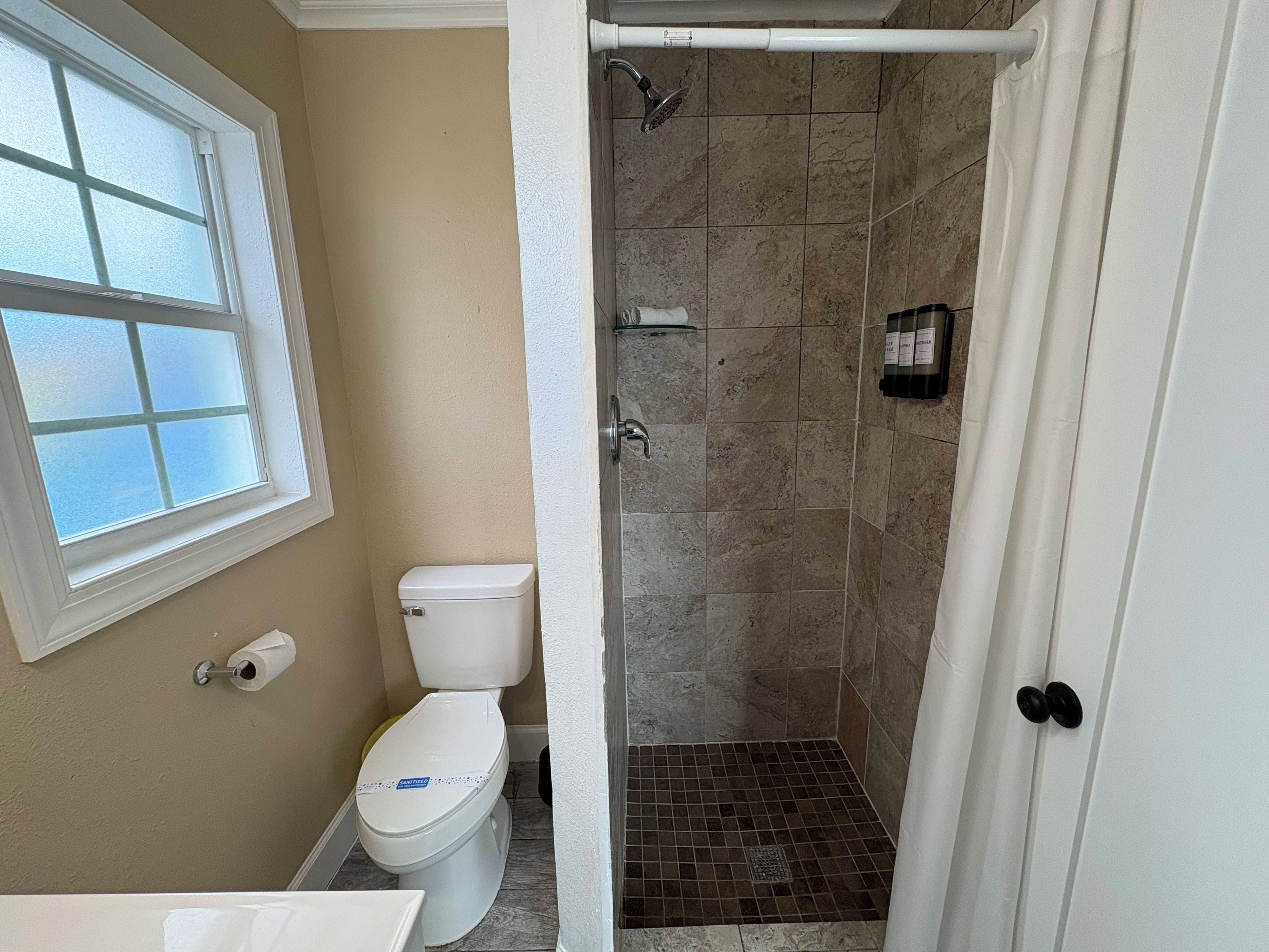 Une salle de bain avec des toilettes, un espace douche et une fenêtre.