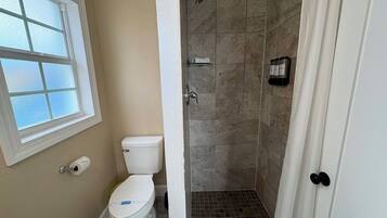 Une salle de bain avec des toilettes, un espace douche et une fenêtre.