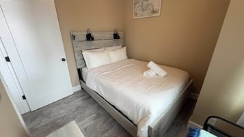 A bedroom with a wooden bed, white bedding, a painting on the wall, and a door.