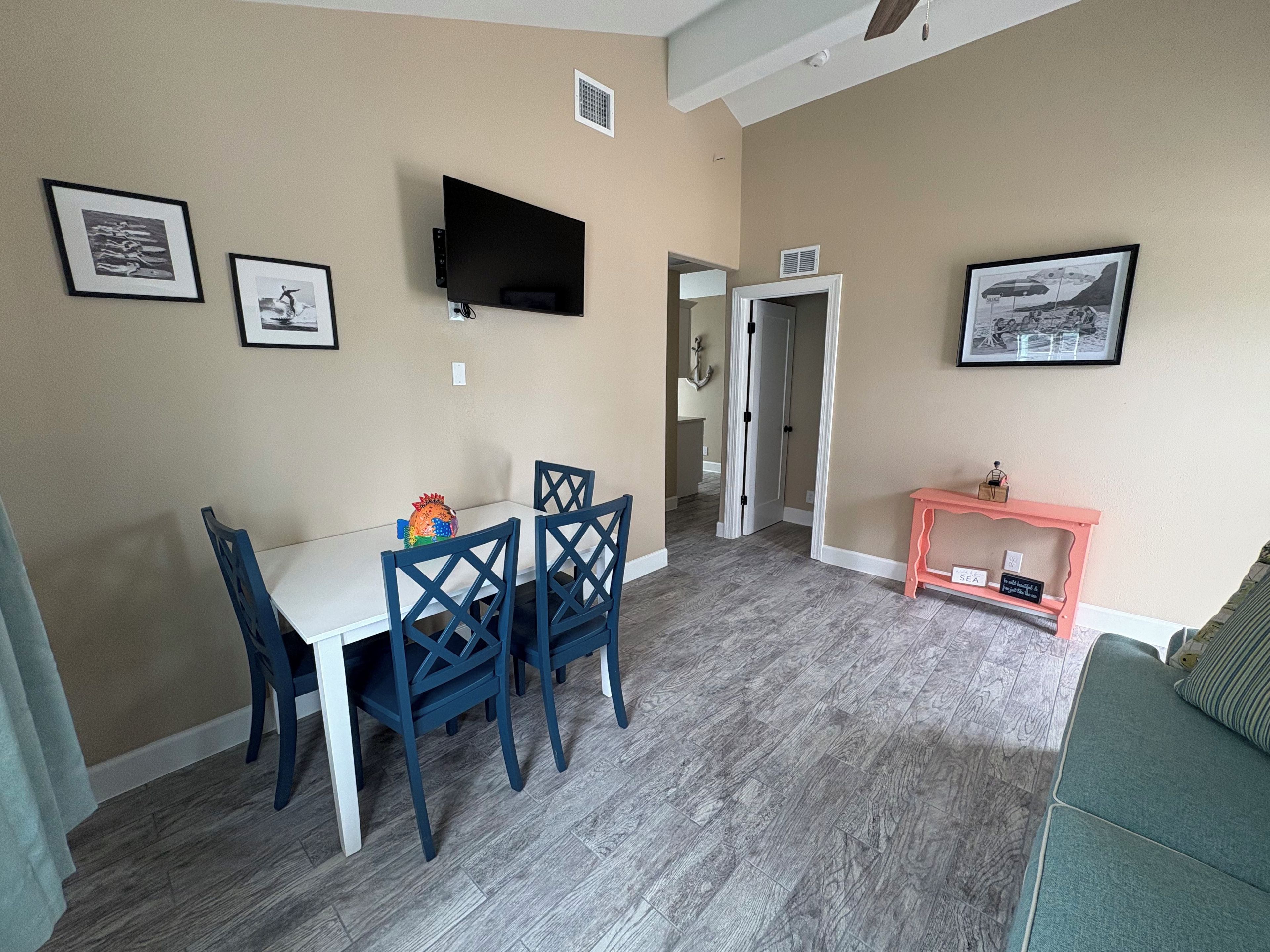 Un coin repas avec une table et des chaises, un téléviseur fixé au mur et une petite console sur laquelle sont disposés des objets décoratifs.