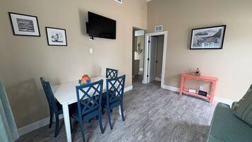 Un coin repas avec une table et des chaises, un téléviseur fixé au mur et une petite console sur laquelle sont disposés des objets décoratifs.