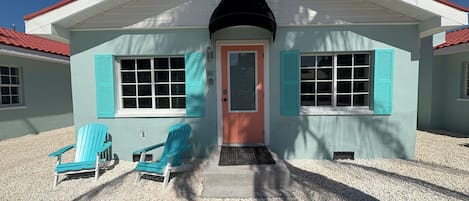 Una casa con puerta roja, contraventanas turquesa y dos sillas Adirondack turquesa en el frente.