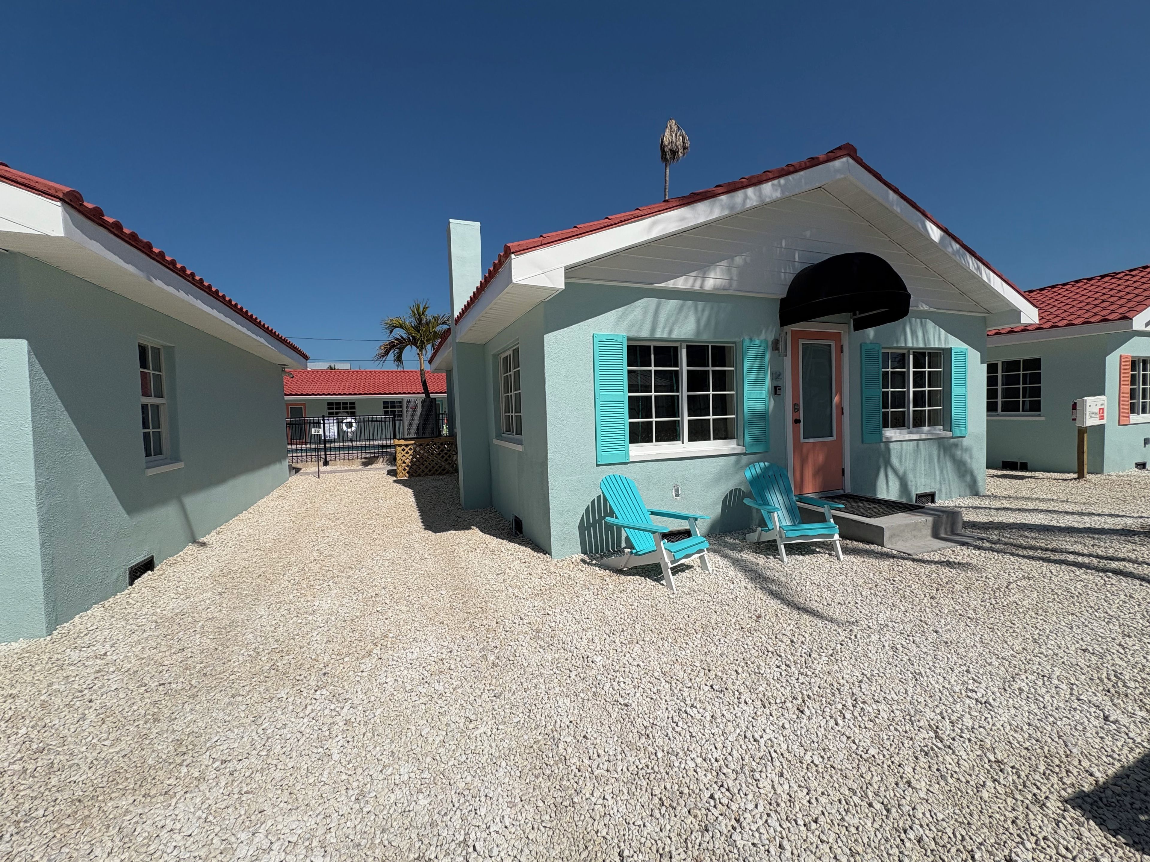 Un bâtiment avec un toit rouge, des volets turquoise et une allée gravillonnée.