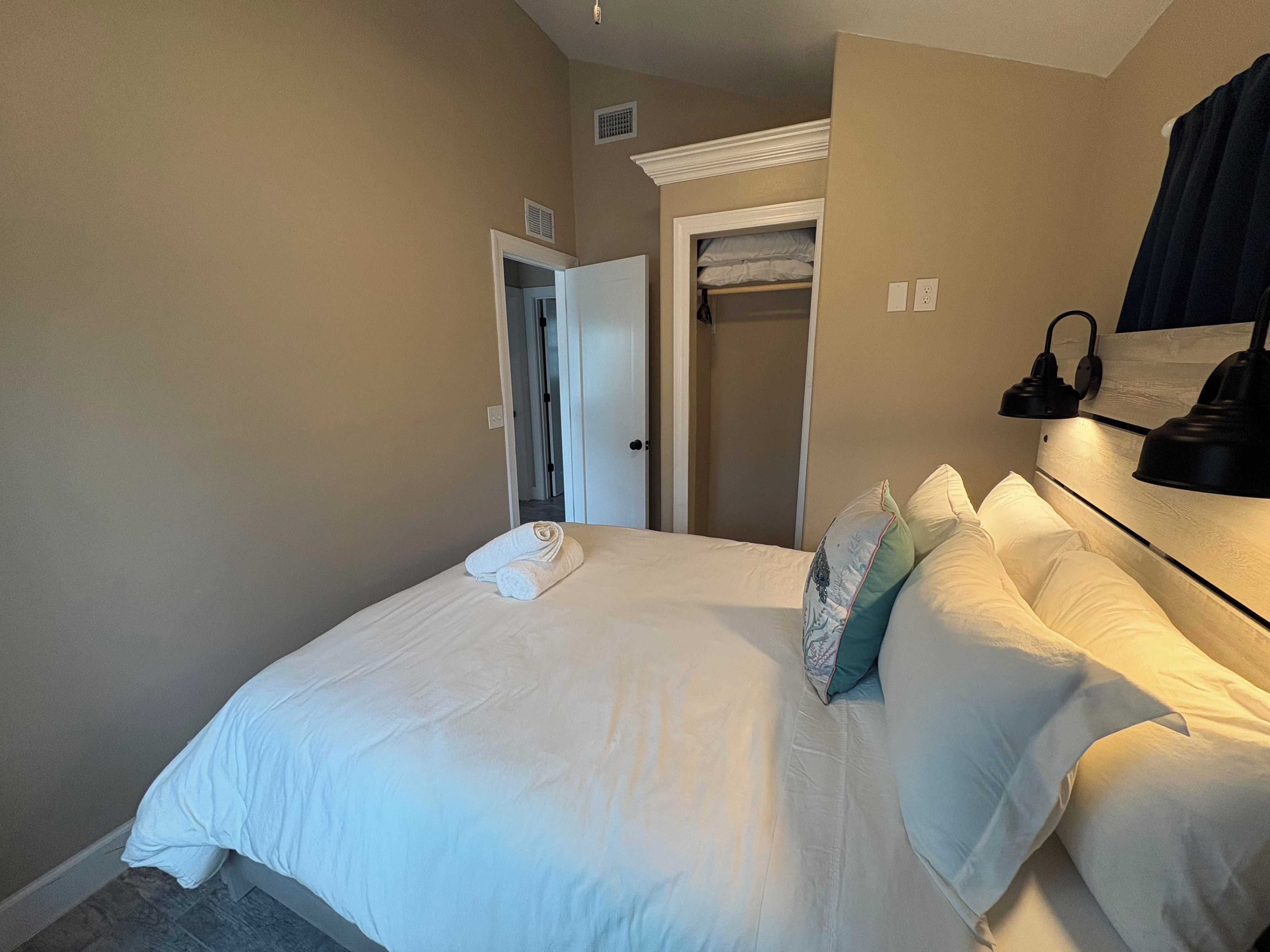Een hotelkamer met een opgemaakt bed, een inloopkast en een bedlampje.