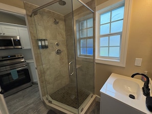Une salle de bain avec une douche à parois de verre, un lavabo blanc et une fenêtre.