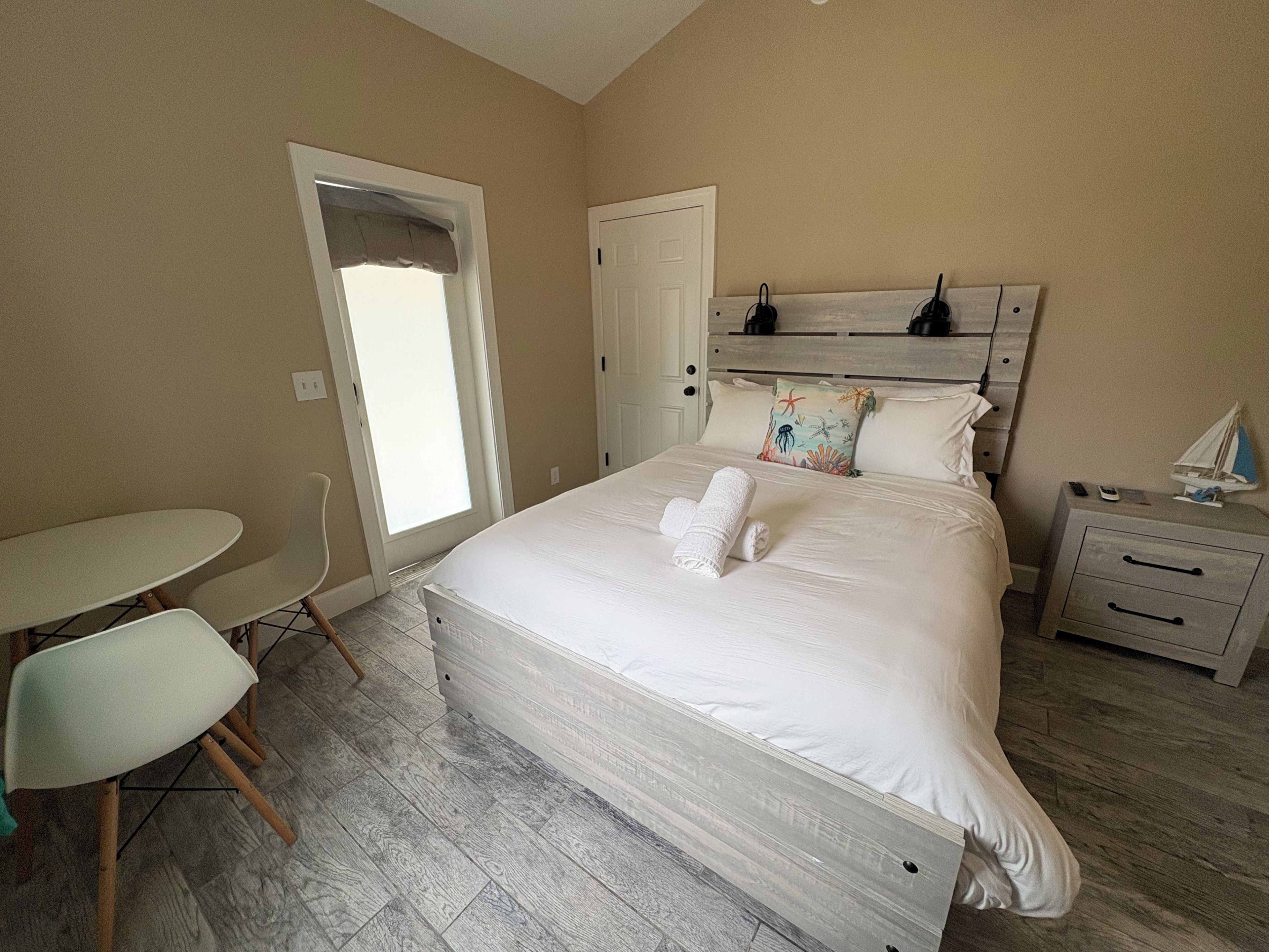 A bedroom with a bed, bedside table, nightstand, chair, and a window with a view.