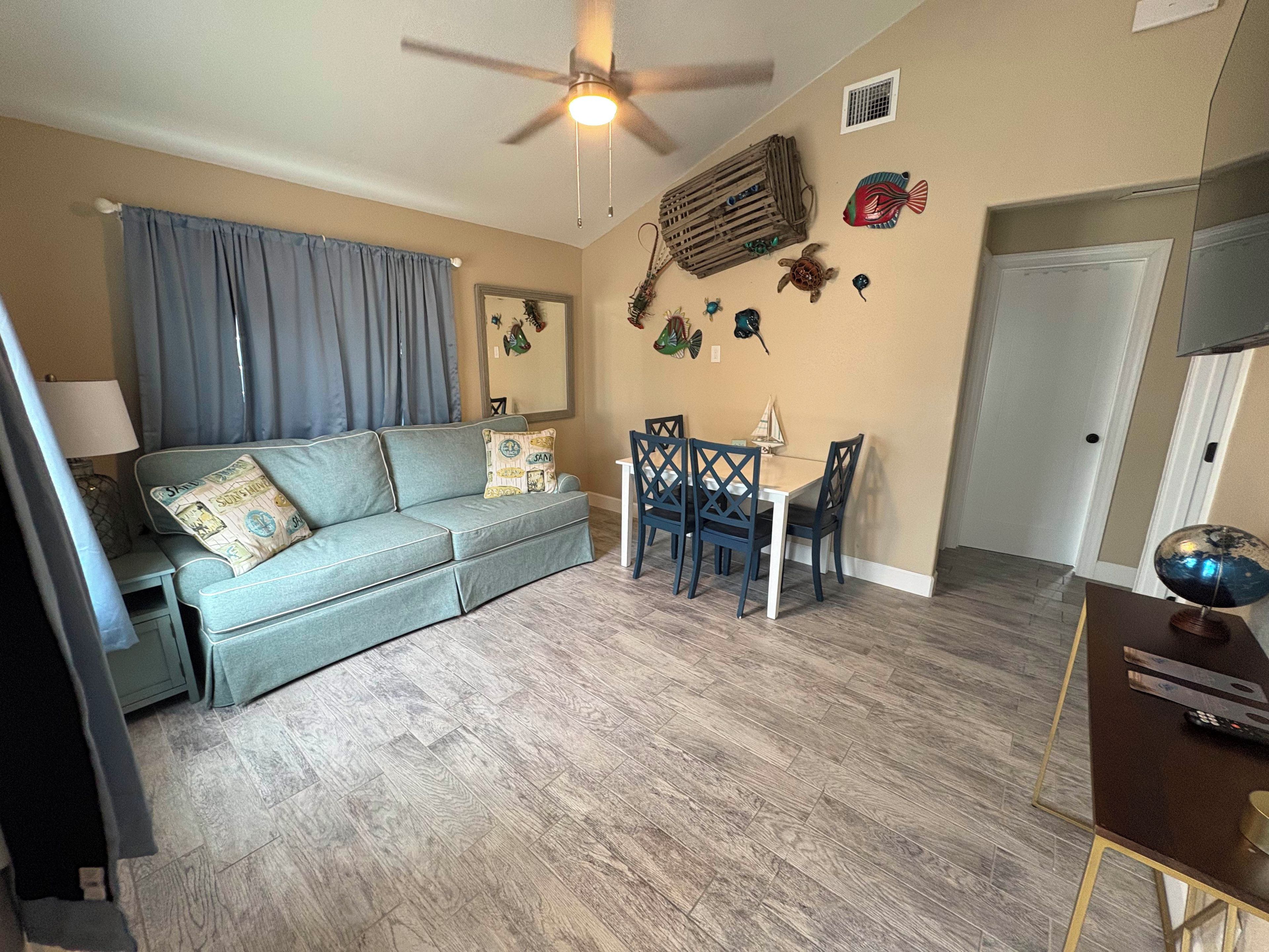 Un salon comprenant un canapé, une table à manger, des chaises, un ventilateur de plafond et des éléments de décoration murale.