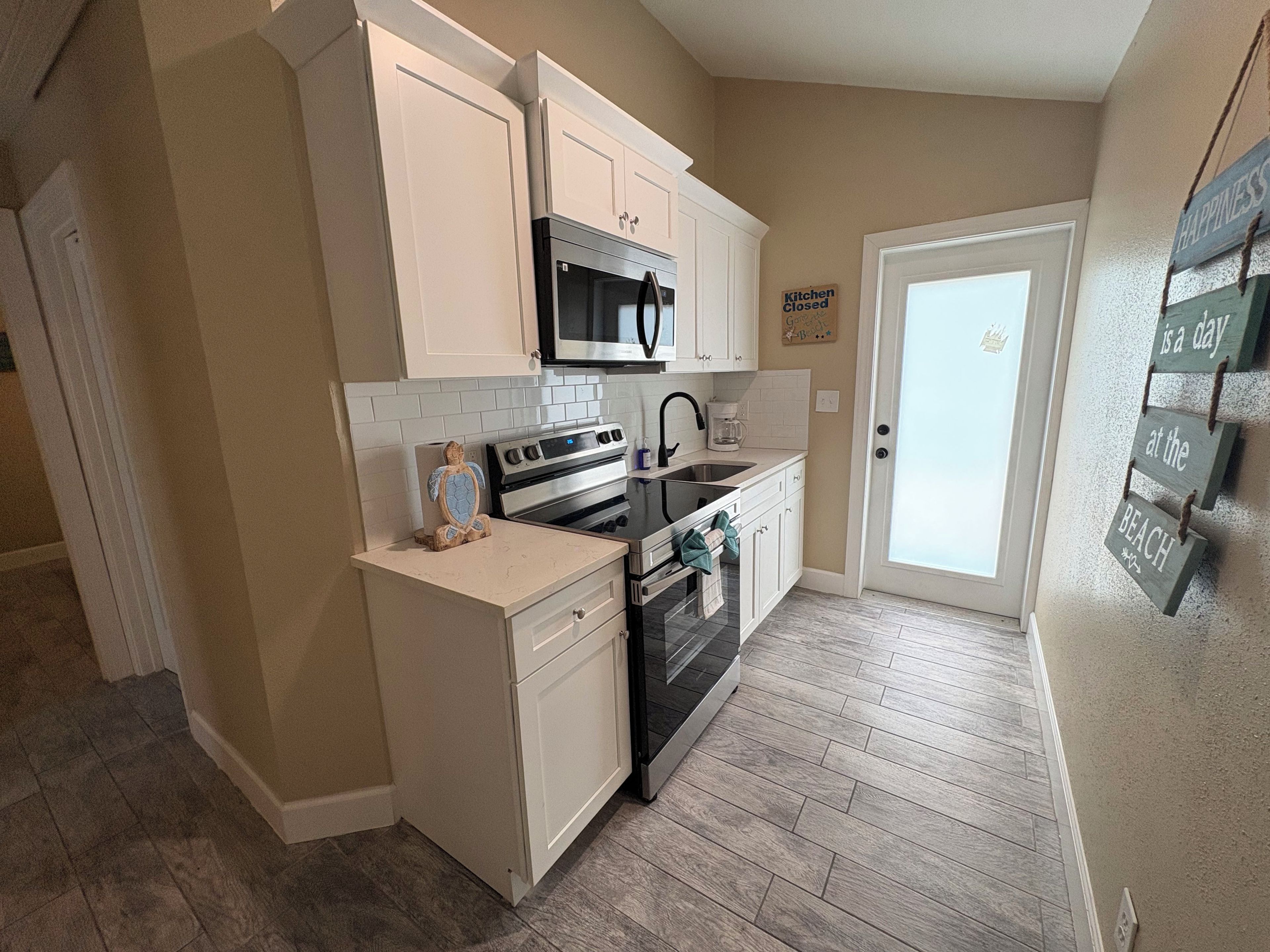 A compact kitchen with white cabinetry, a microwave, a stove, and a sink.