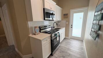 A compact kitchen with white cabinetry, a microwave, a stove, and a sink.