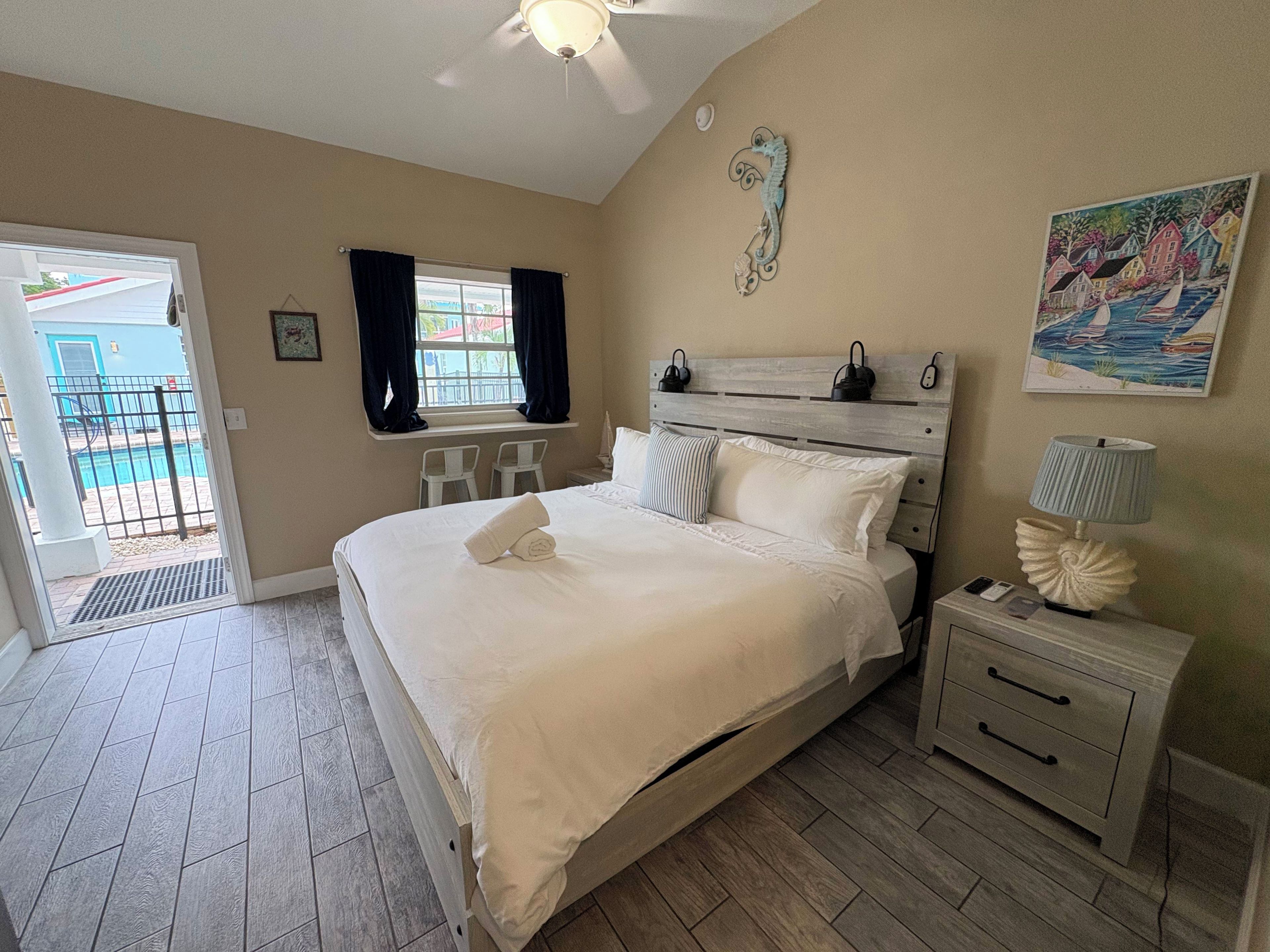 A bedroom with a bed, bedside tables, a window with curtains, a ceiling fan, and a painting on the wall.