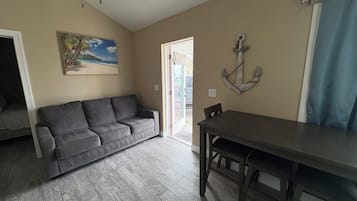 Un salon avec un canapé gris, une table à manger en bois et un tableau représentant une scène de plage.