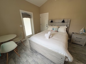 A bedroom with a bed, bedside table, nightstand, chair, and a window with a view.