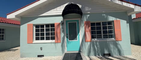Un edificio con fachada azul claro, contraventanas rojas y puerta blanca.