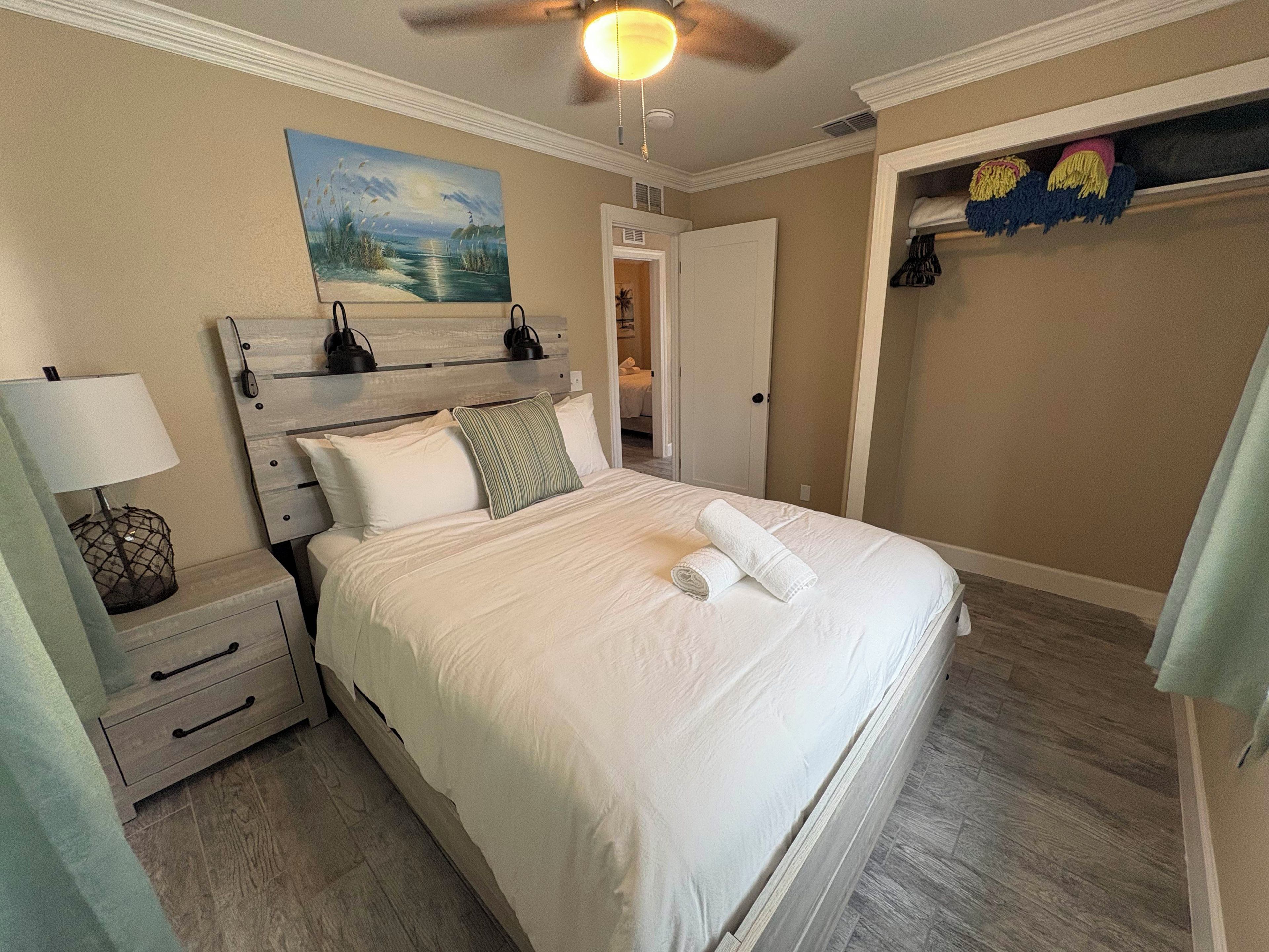 A bedroom with a bed, nightstand, lamp, painting, closet, and a ceiling fan.