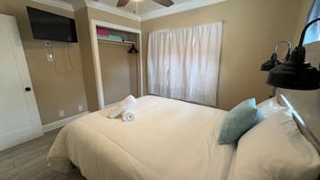 Une chambre d’hôtel avec un lit, un ventilateur de plafond, une télévision, un placard et une fenêtre avec des rideaux.