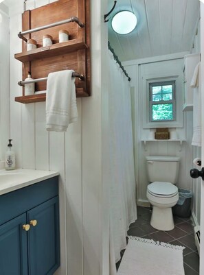 Un baño con un estante de madera, un inodoro blanco, una ventana y un armario azul.