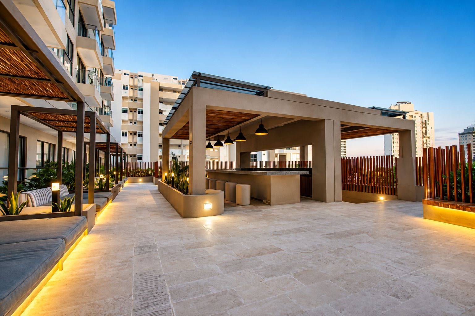 A modern outdoor lounge area with seating and a bar, surrounded by high-rise buildings.