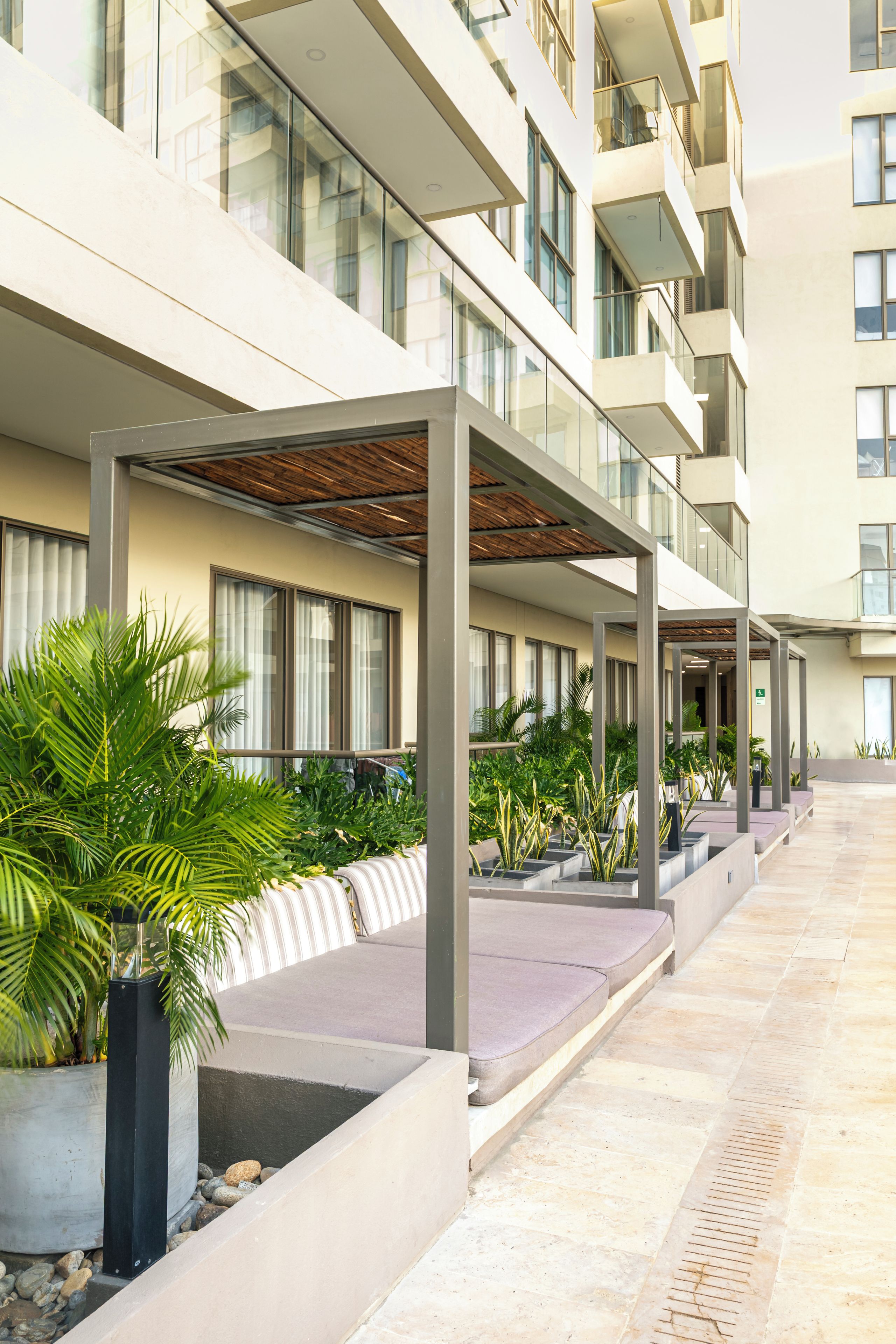 A modern hotel corridor with multiple floors, covered outdoor seating areas, and potted plants.