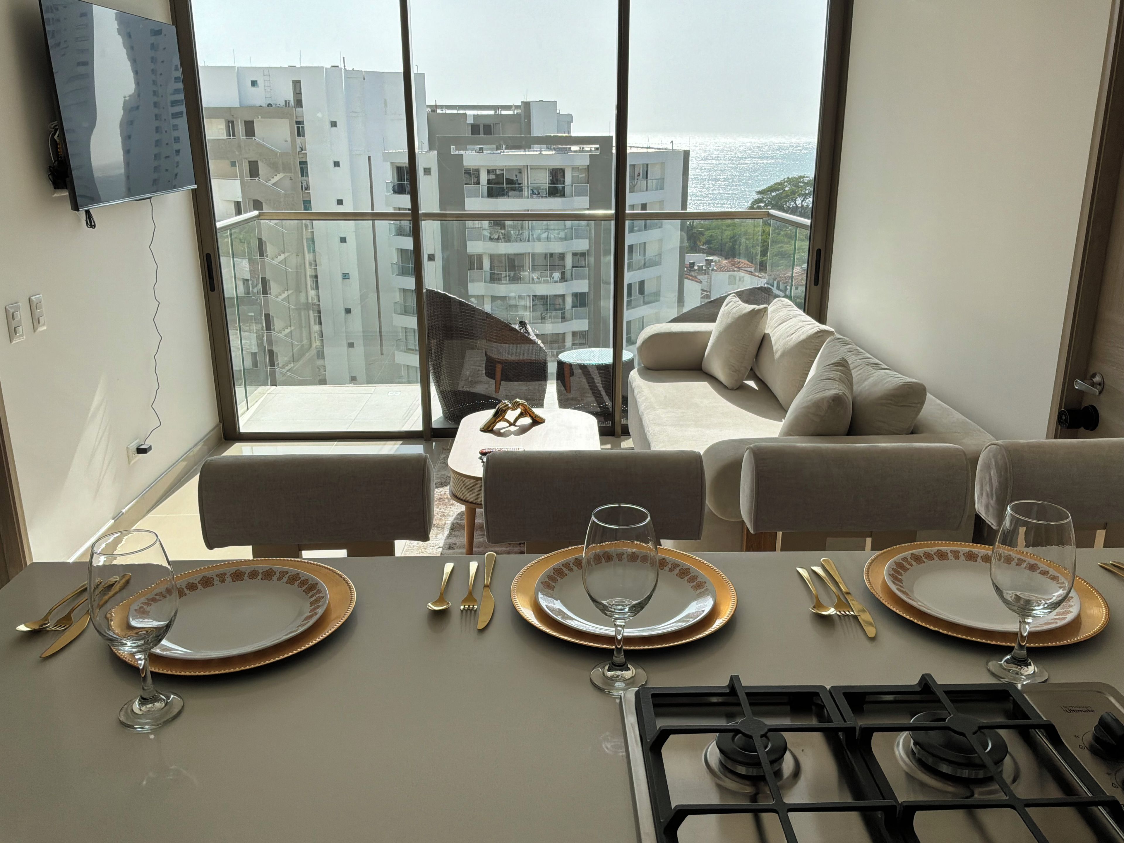 Een moderne woonkamer met balkon, een bank, een eettafel voor twee personen en een aan de muur bevestigde televisie.