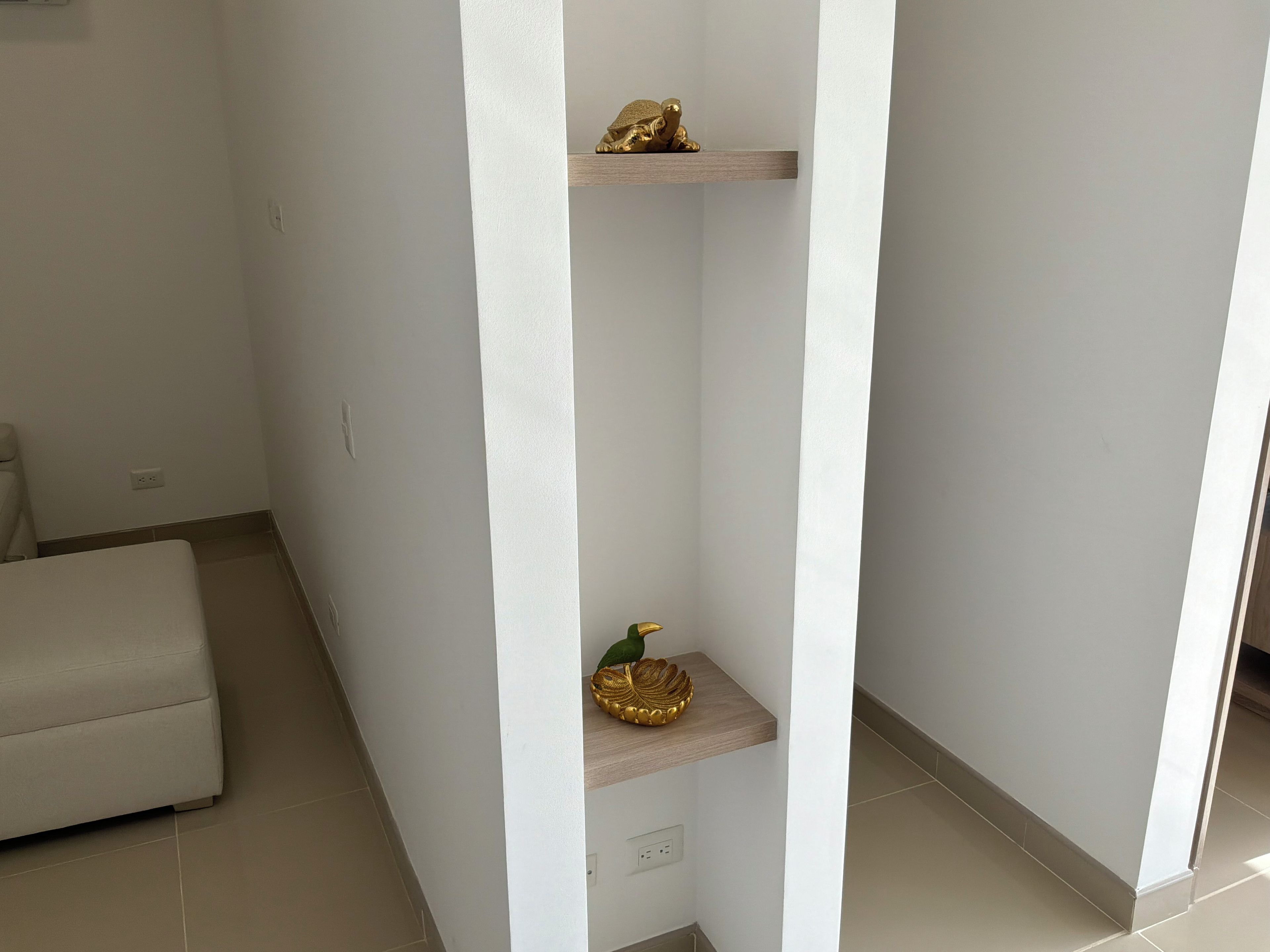 A room with a white wall, a wooden floor, a white sofa, and a white pillar with shelves.