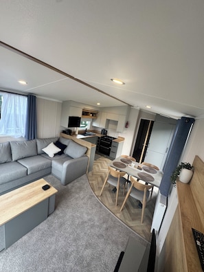A compact living space with a sofa, a dining table, and a kitchenette. - St Andews Brand New - 3 Bedroom Luxury Caravan (St Andrews)