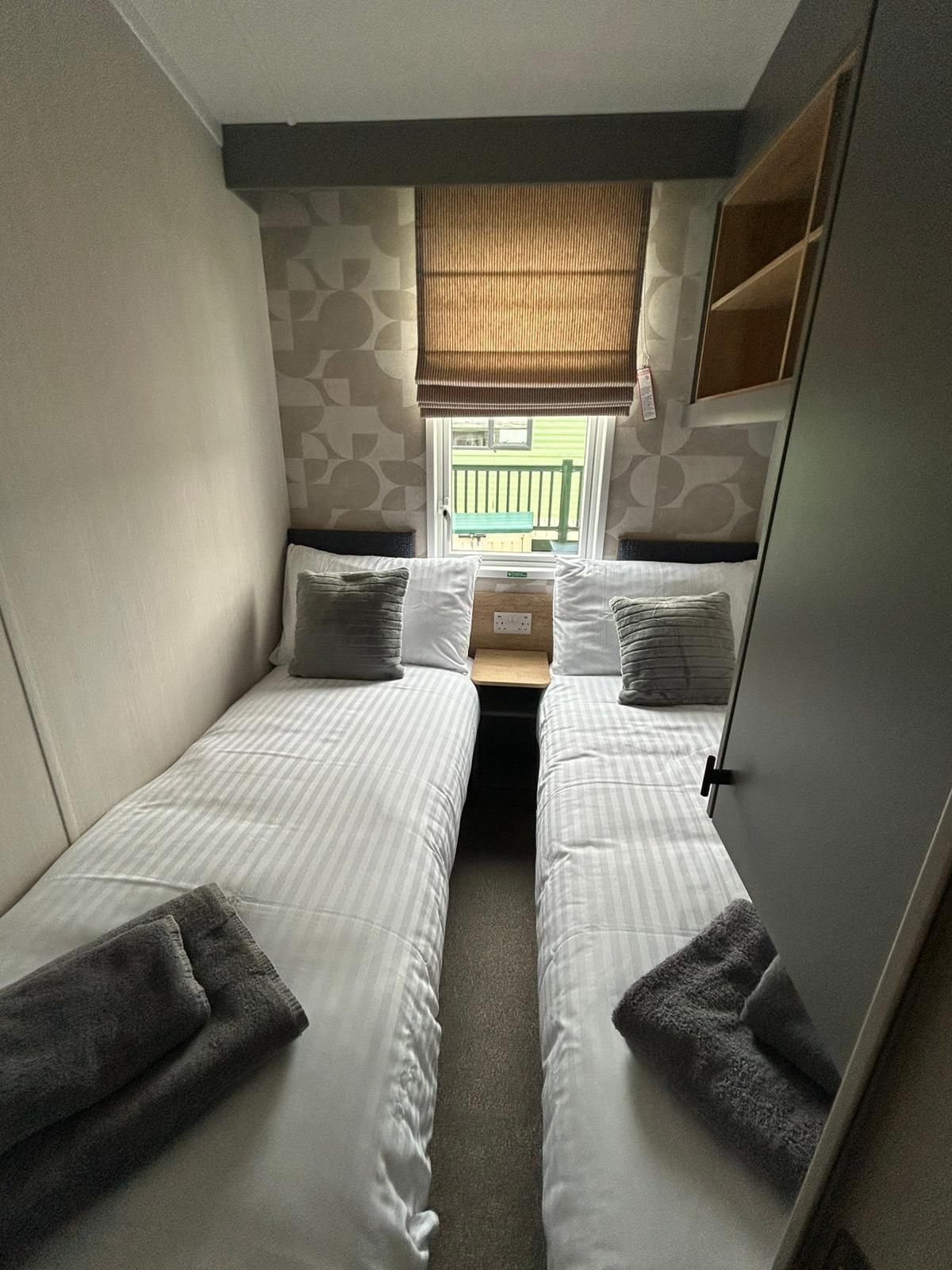 Una habitación compacta con dos camas individuales, una ventana con persianas y una mesita.