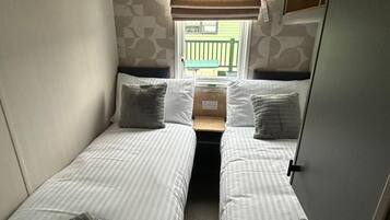 Una habitación compacta con dos camas individuales, una ventana con persianas y una mesita.