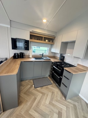 A modern kitchen with grey cabinets, a black stove, and a microwave above the counter. - St Andews Brand New - 3 Bedroom Luxury Caravan (St Andrews)