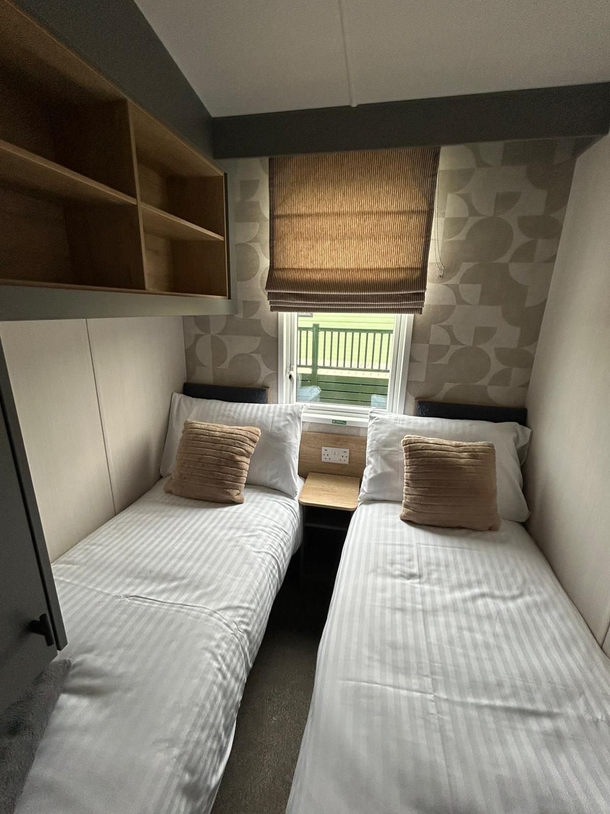 Una habitación compacta con dos camas, una ventana con vistas y una estantería empotrada sobre las camas.