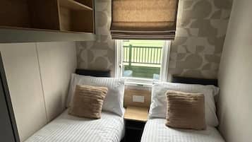 Una habitación compacta con dos camas, una ventana con vistas y una estantería empotrada sobre las camas.