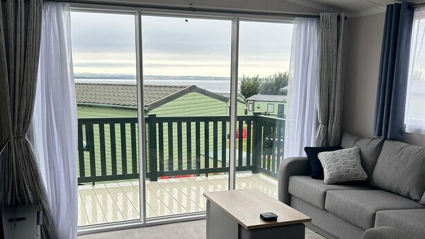 Een moderne woonkamer met een bank, een salontafel en uitzicht op een groen gebouw door grote ramen.