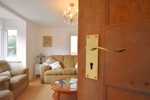 Ein Zimmer mit Holztür, einem beigefarbenen Sofa, einem kleinen Tisch und einer Chandelier.