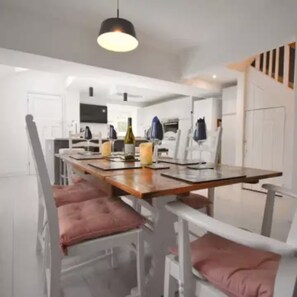 A dining area with a long wooden table, white chairs with pink cushions, and a pendant light above. - Sea-Renity Sidmouth Sleeps 6 Parking for 2 Vehicles (Sidmouth)
