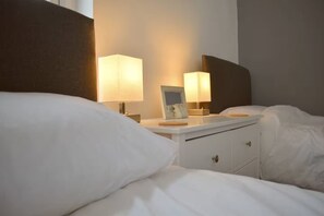 Quarto de hotel com cama, mesas de cabeceira, luminárias e um criado-mudo com porta-retrato.