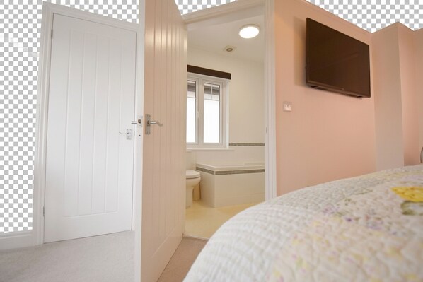 Ein Schlafzimmer mit Bett, einer Tür, einem Badezimmer mit Toilette und Waschbecken sowie einem an der Wand befestigten Fernseher.