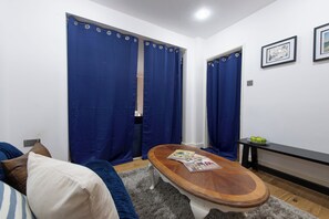 Ein Zimmer mit einer Couch, einem Couchtisch mit Zeitschriften, einem blauen Vorhang und einem gerahmten Bild an der Wand.