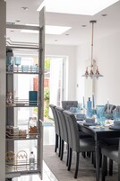 Uma área de jantar moderna com despensa de frente para o vidro, mesa de jantar posta com copos azuis e luminária pendente.