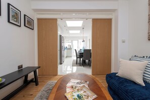 Uma sala de estar moderna com sofá, mesa de centro com revistas, um banco e uma área de refeições ao fundo.