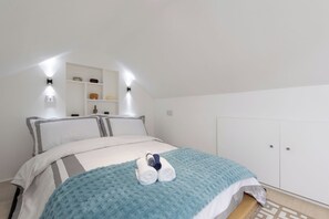 Ein Schlafzimmer mit einem Bett, einer blauen Decke und einem zusammengerollten Handtuch. Es gibt Wandleuchten und ein Regal mit Dekoration.