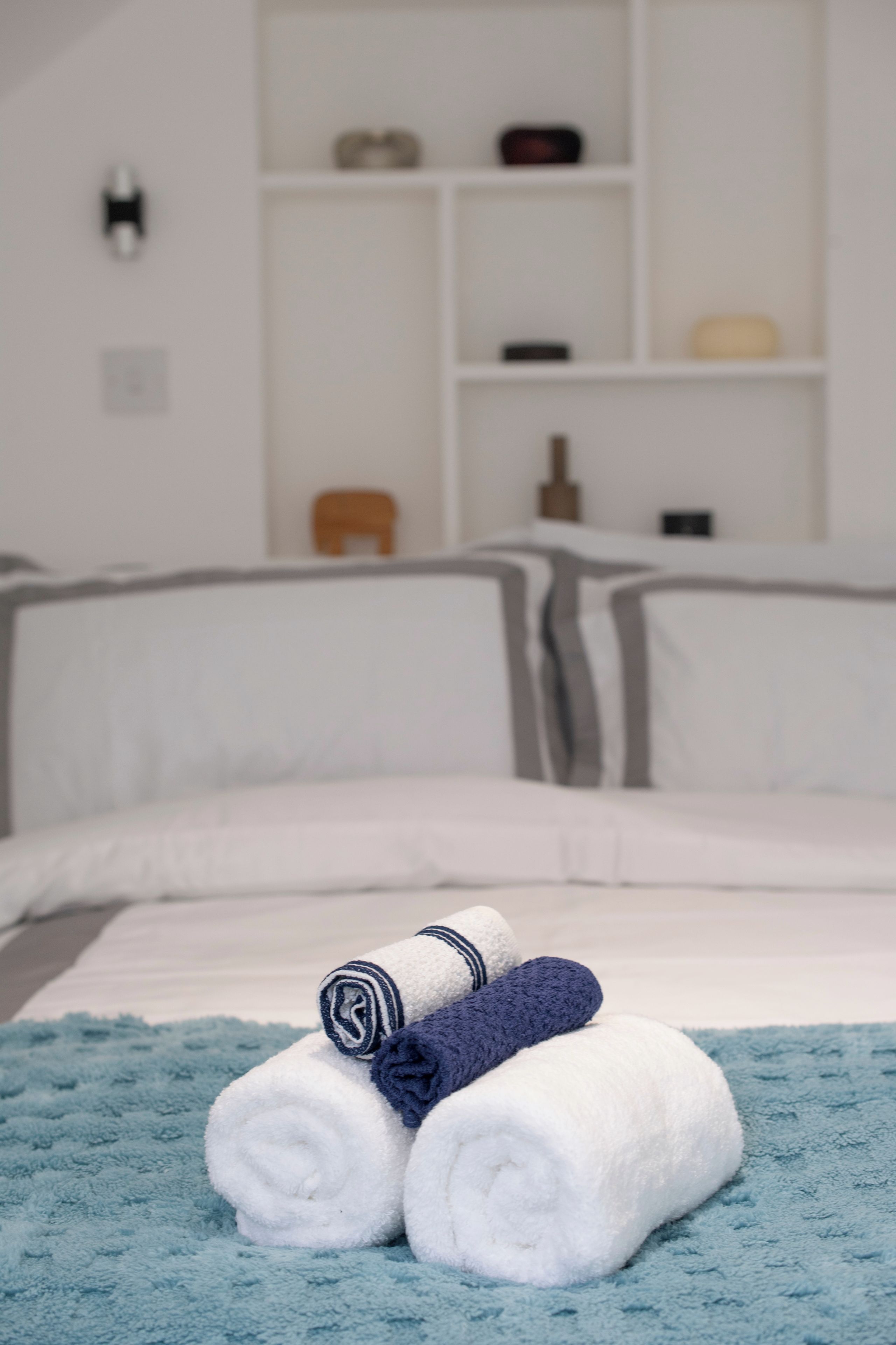 Un lit bien fait, avec des serviettes blanches et bleu marine enroulées, une couverture bleue à texture et une tête de lit blanche.