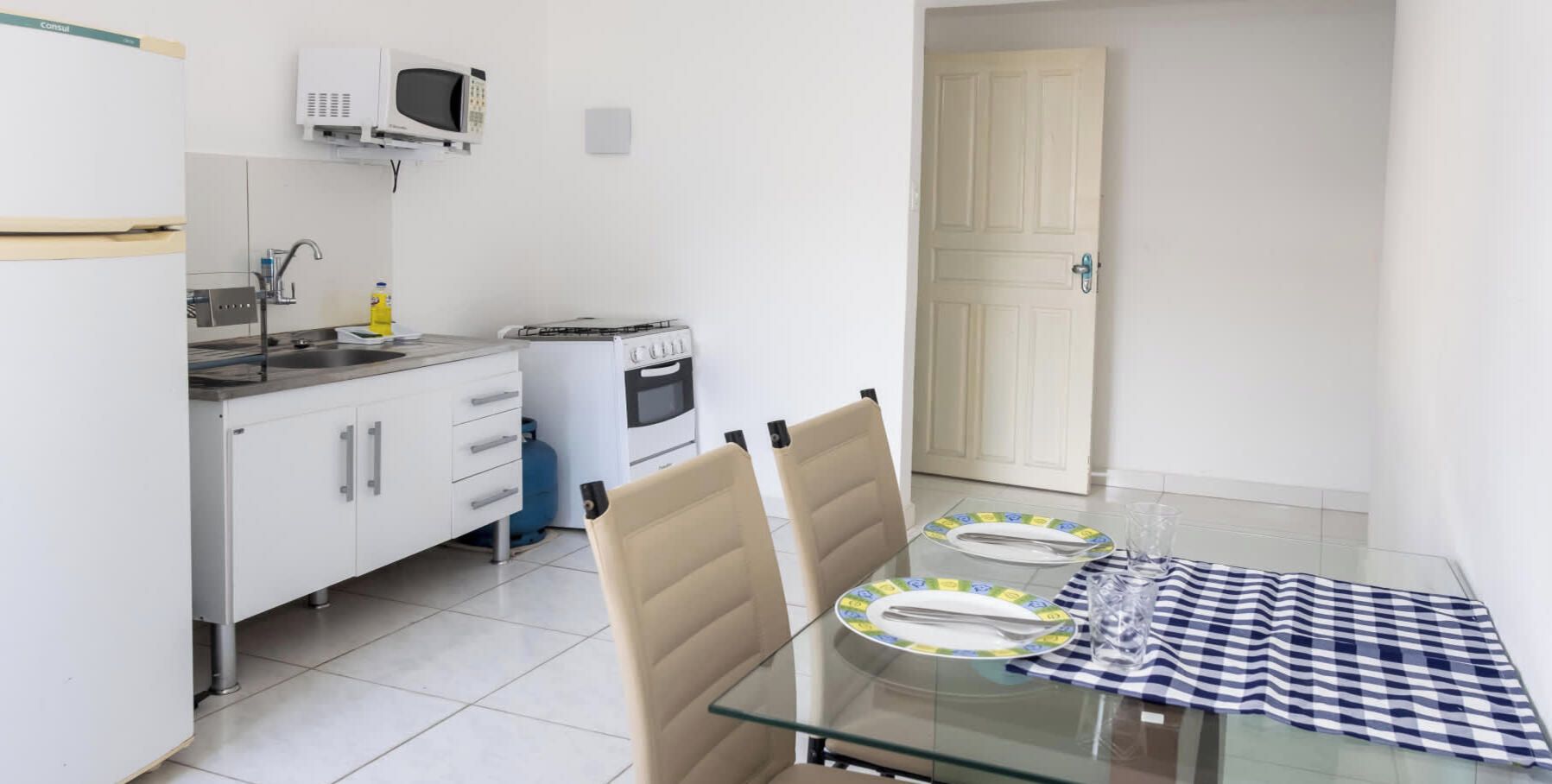 A small kitchen with a microwave, stove, and gas stove. There is a dining table with chairs and a checkered tablecloth.
