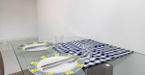 Ein Esstisch mit zwei Tellern, Besteck und Gläsern auf einer Glastischplatte, vor einer weißen Wand.